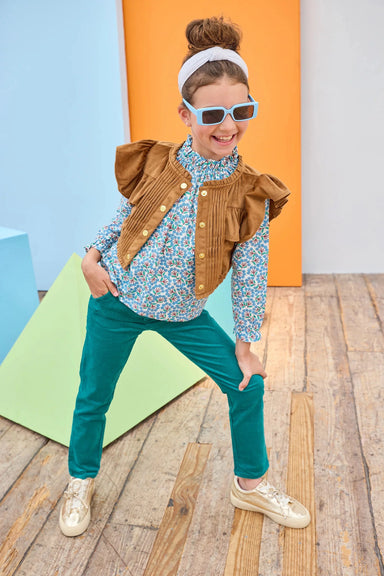 Child wearing a brown jacket and blue pants on a wooden floor with colorful background