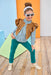 Child wearing a brown jacket and blue pants on a wooden floor with colorful background