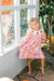Young girl wearing a pink and orange floral dress with autumn turkey accents by Poppy Kids beside a bright window