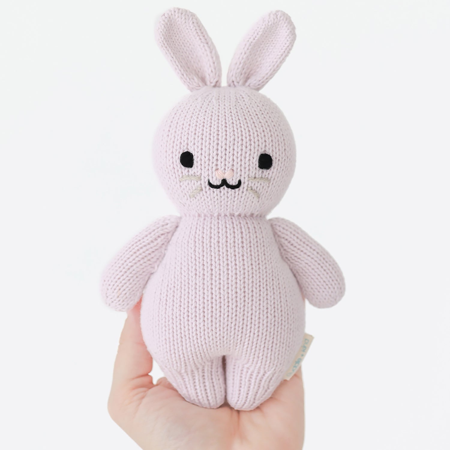 Knitted rabbit toy held in a hand against a white background