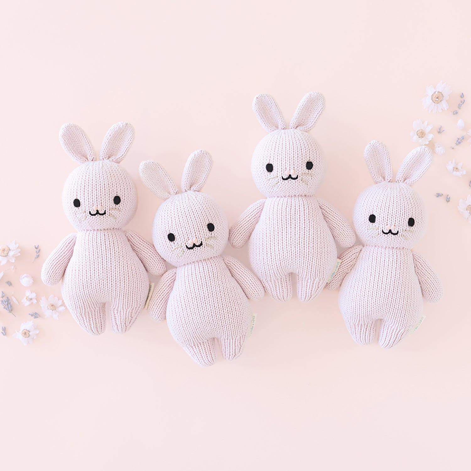 Four white knit bunny toys on a light pink background