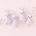 Four white knit bunny toys on a light pink background