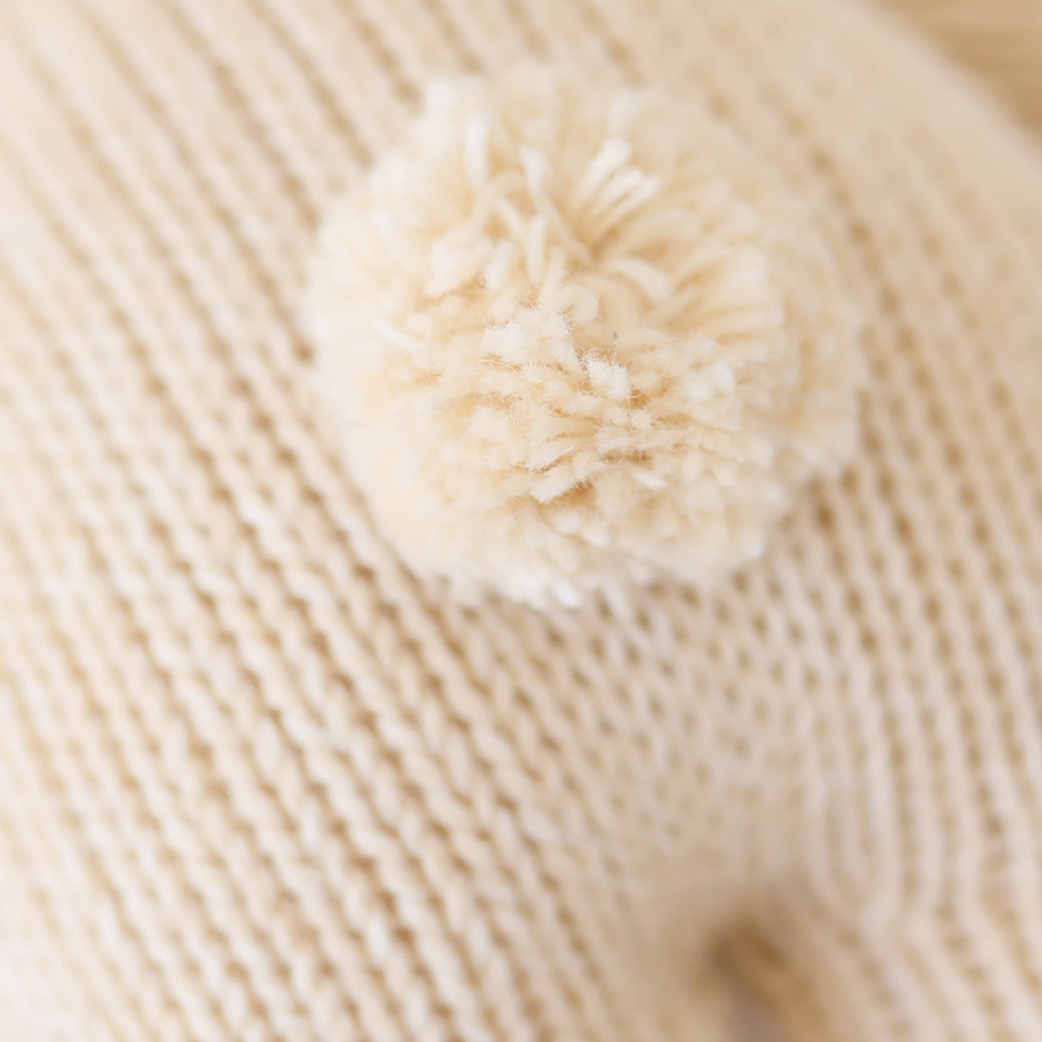 Close-up of a ball of cream-colored yarn on a textured beige surface.