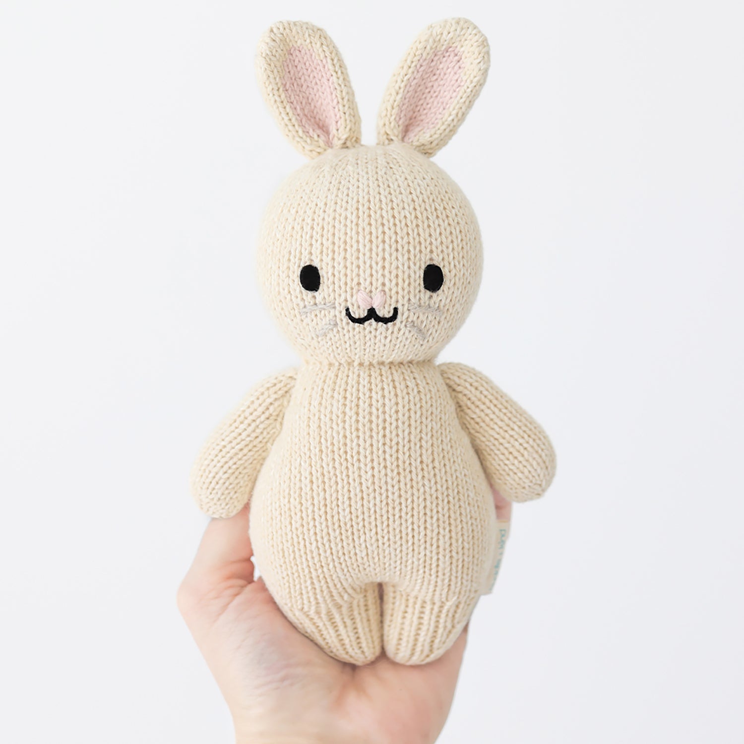 Knitted bunny toy held in a hand against a white background