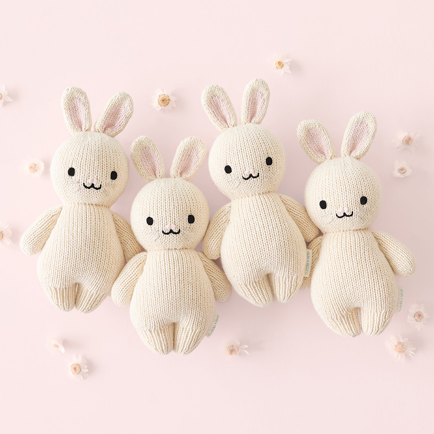 Four knitted bunny toys on a pink background
