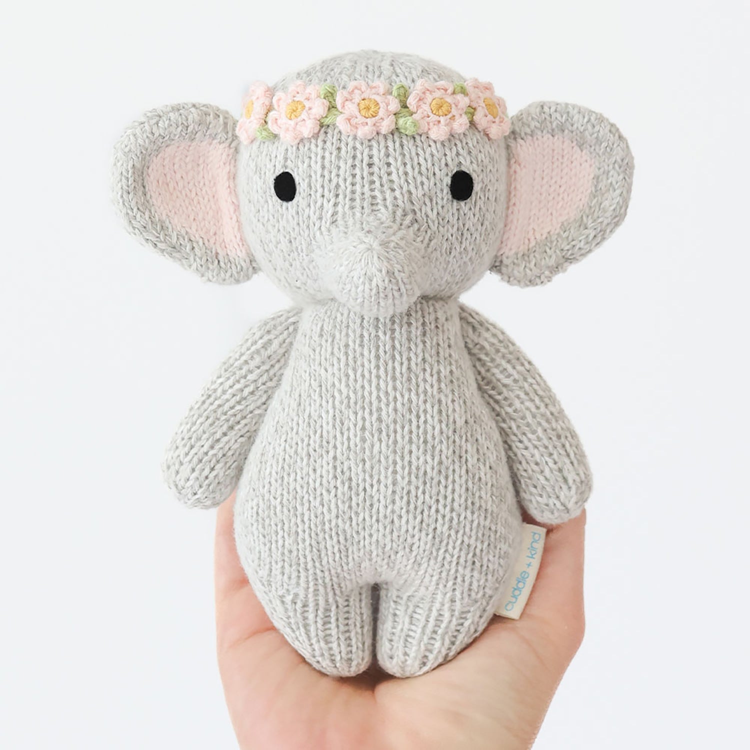 Knitted elephant toy with a flower crown held in a hand on a white background