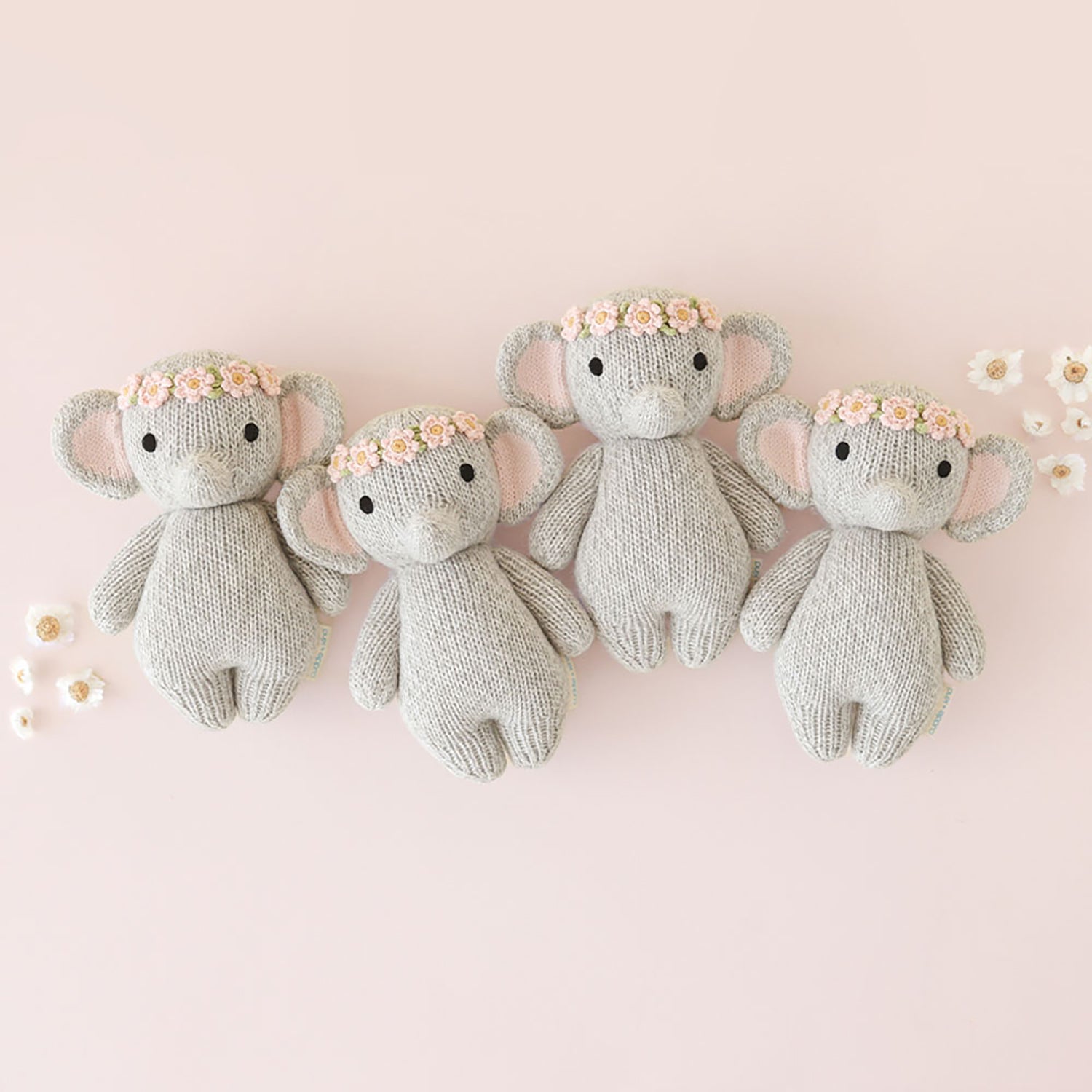 Four knitted elephant toys with flower crowns on a pink background