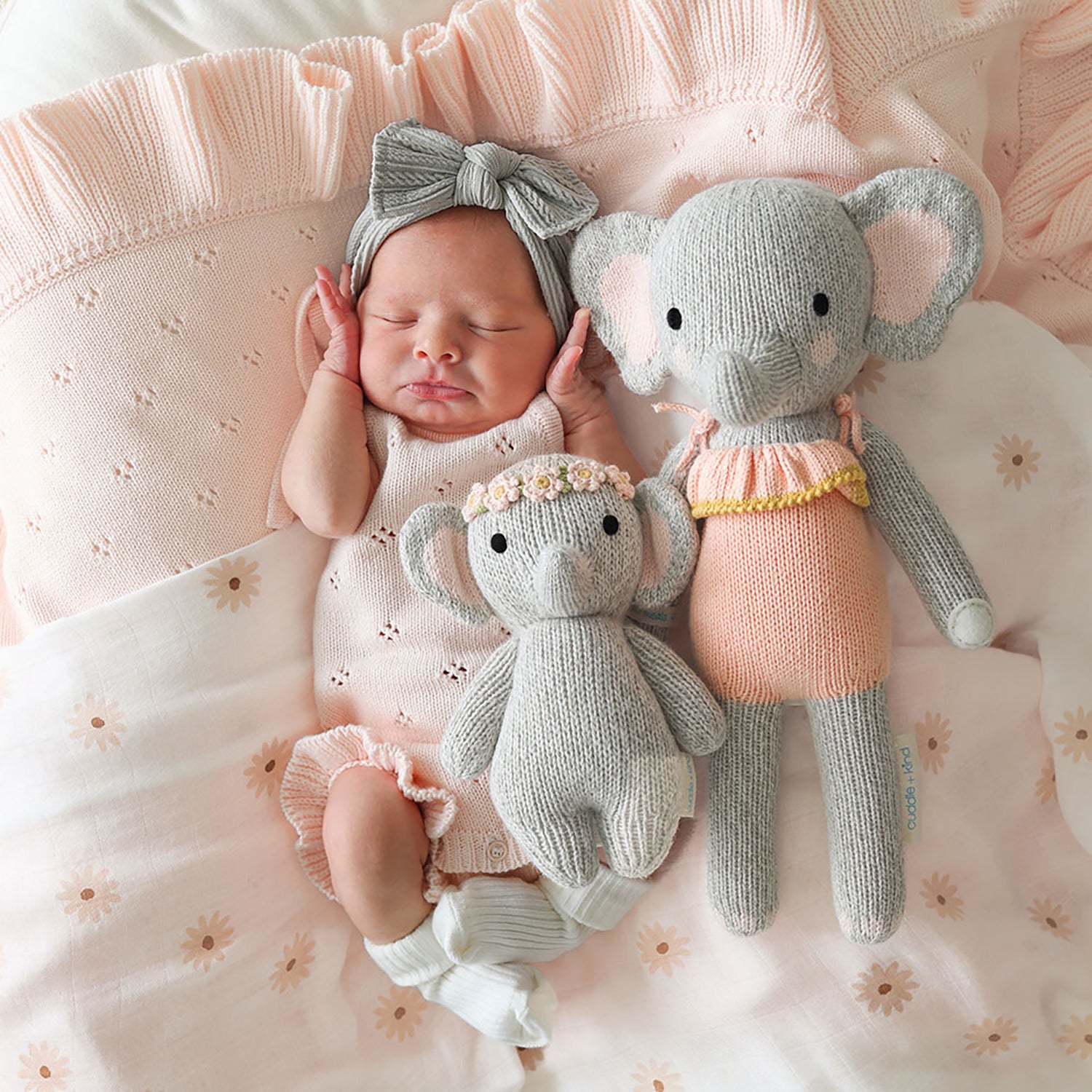 Newborn baby girl lying on a pink blanket with two knitted elephant toys.