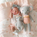 Newborn baby girl lying on a pink blanket with two knitted elephant toys.
