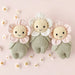 Three knitted flower dolls on a pink background with small flowers around them.