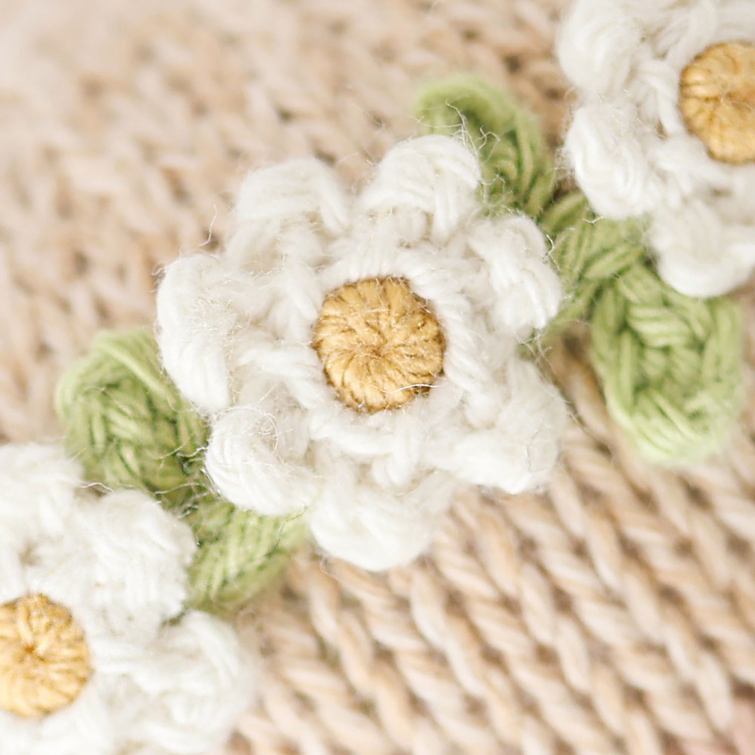Close-up of white and green knitted flowers on a textured beige background