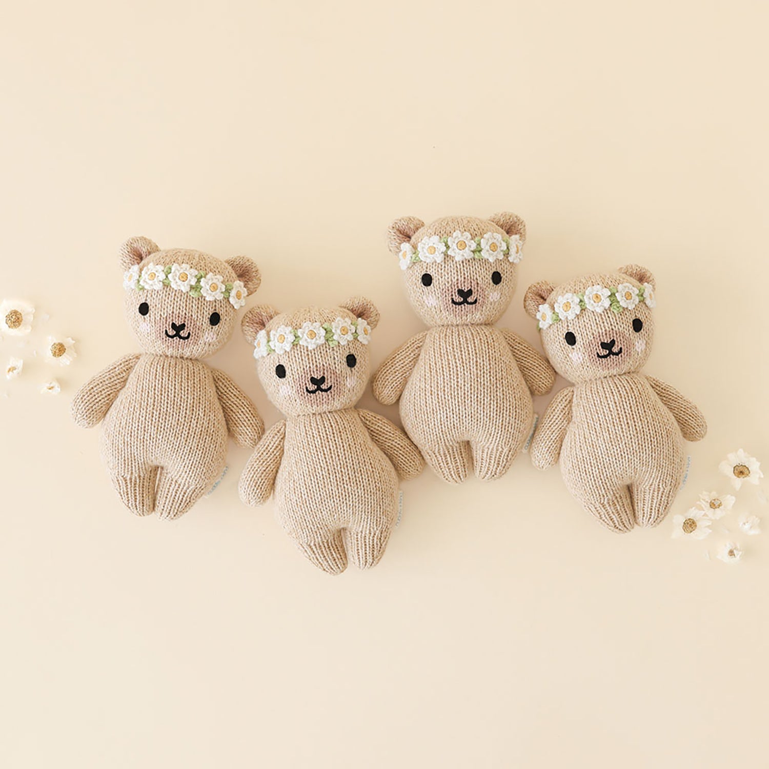 Four knitted teddy bears with floral headbands on a light beige background