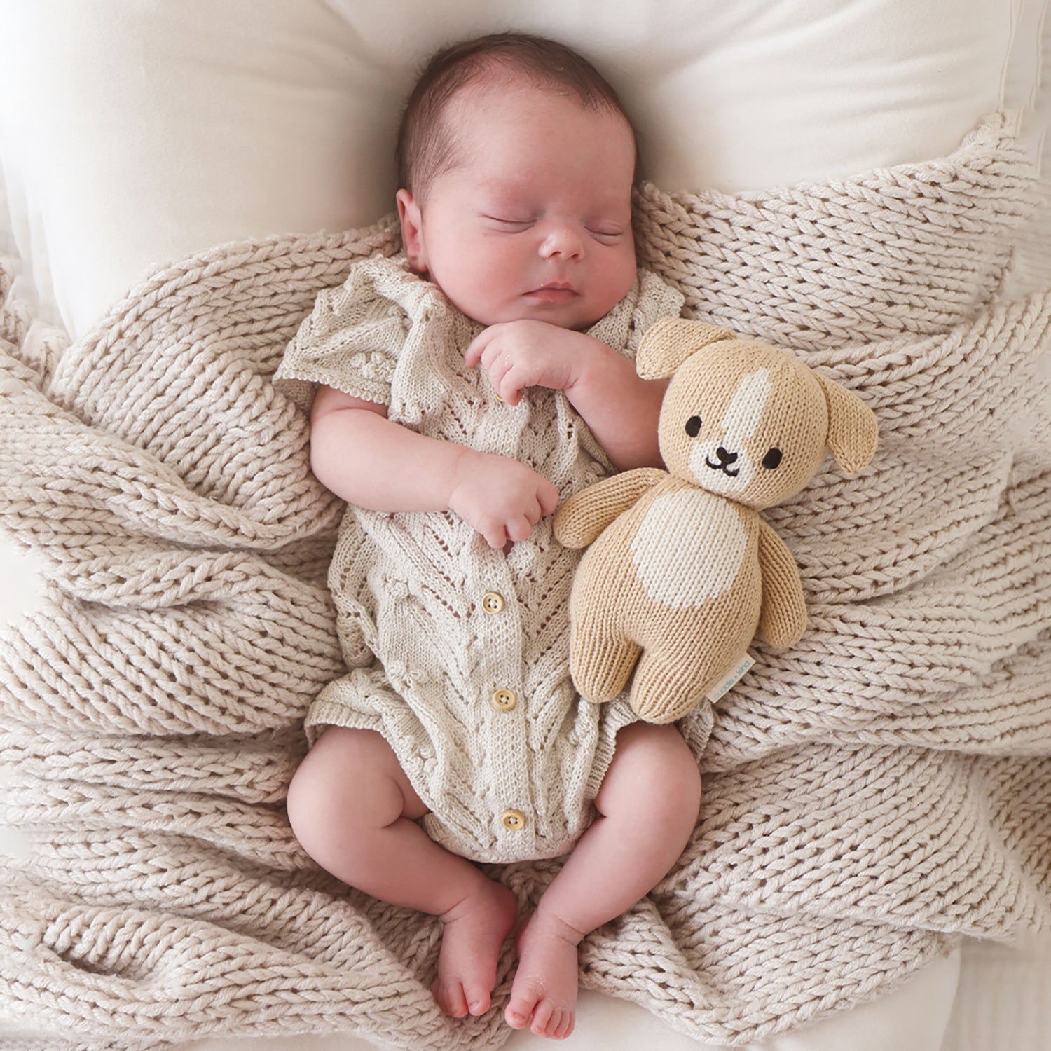 Newborn baby in a knitted outfit holding a teddy bear on a textured blanket