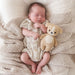 Newborn baby in a knitted outfit holding a teddy bear on a textured blanket