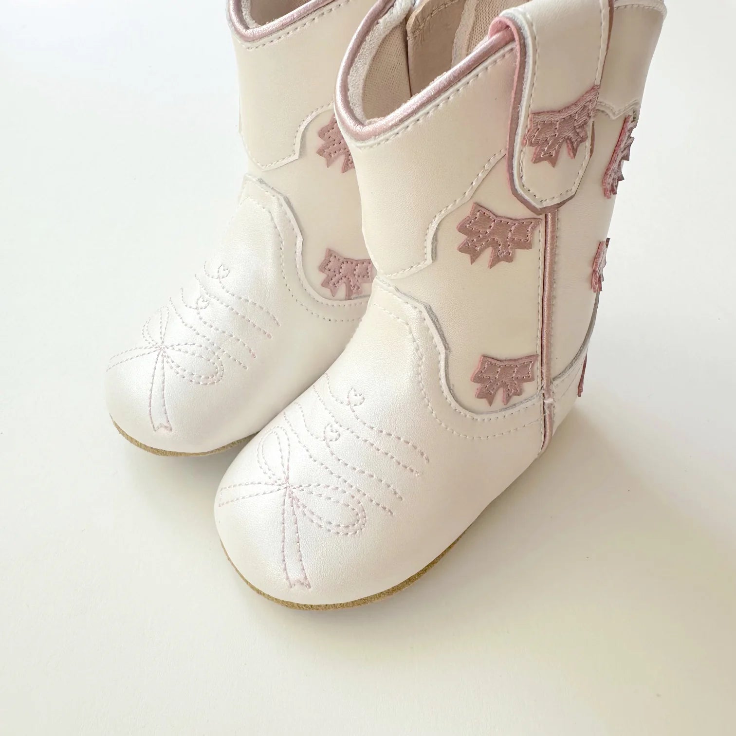 White children's cowboy boots with pink floral patterns on a light background
