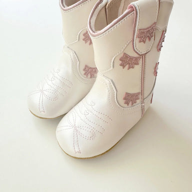 White children's cowboy boots with pink floral patterns on a light background