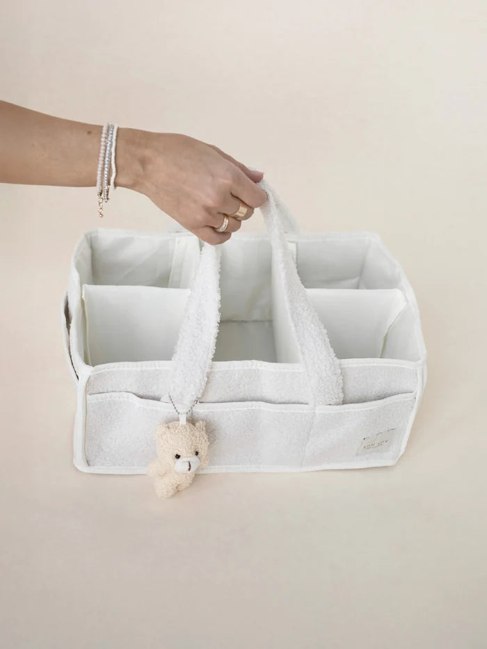 White storage caddy with a teddy bear toy held by a hand on a beige background