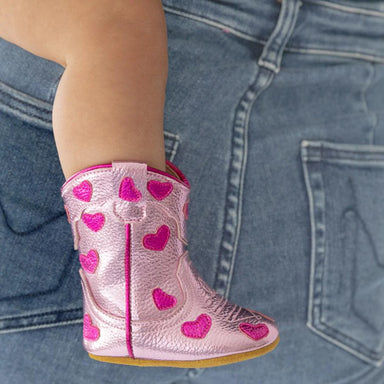 Pink cowboy boot with heart patterns worn by a child against blue jeans.
