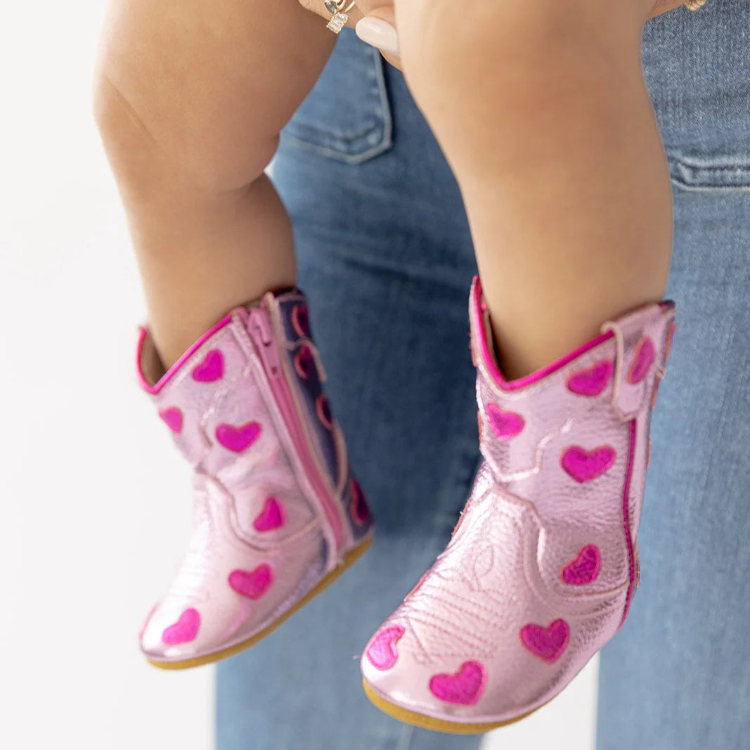 Pink rain boots with heart patterns worn by a child, held by an adult wearing blue jeans.