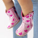 Pink cowboy boots with heart patterns worn by a child on a light blue background