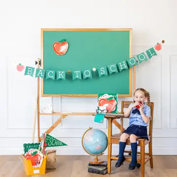 Child sitting at a desk with a 'Back to School' banner and supplies in a classroom setting.