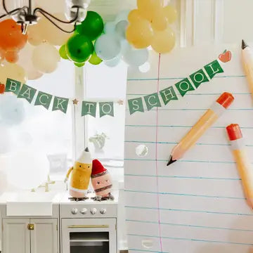 Decorative setup with 'Back to School' banner, balloons, and stationery items in a kitchen.