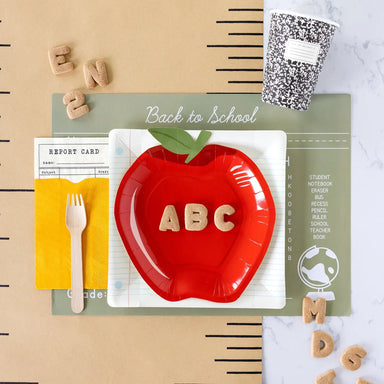 Red apple-shaped plate with 'ABC' letters on a back-to-school themed background with a black and white composition cup