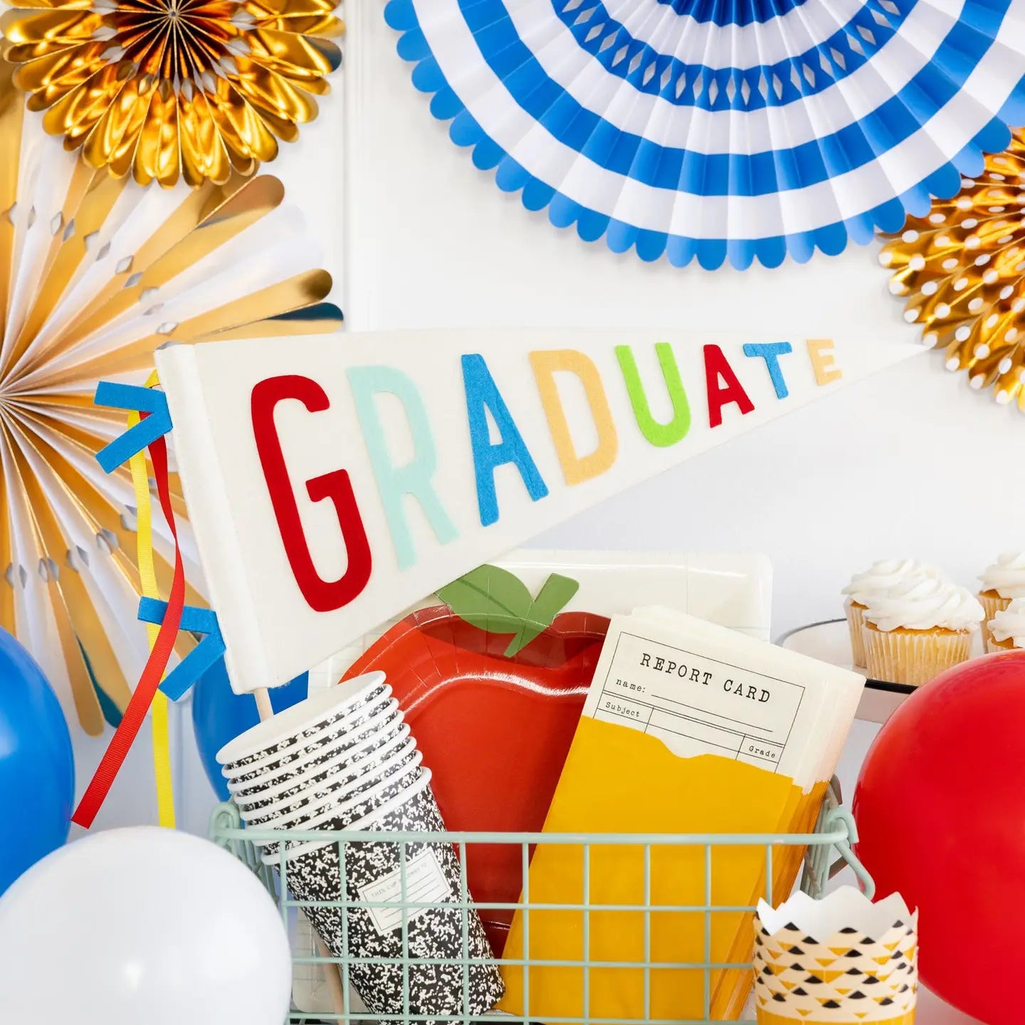 Graduation-themed decorations with 'GRADUATE' sign, balloons, composition cups, and party supplies on a white background.