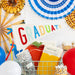 Graduation-themed decorations with 'GRADUATE' sign, balloons, composition cups, and party supplies on a white background.