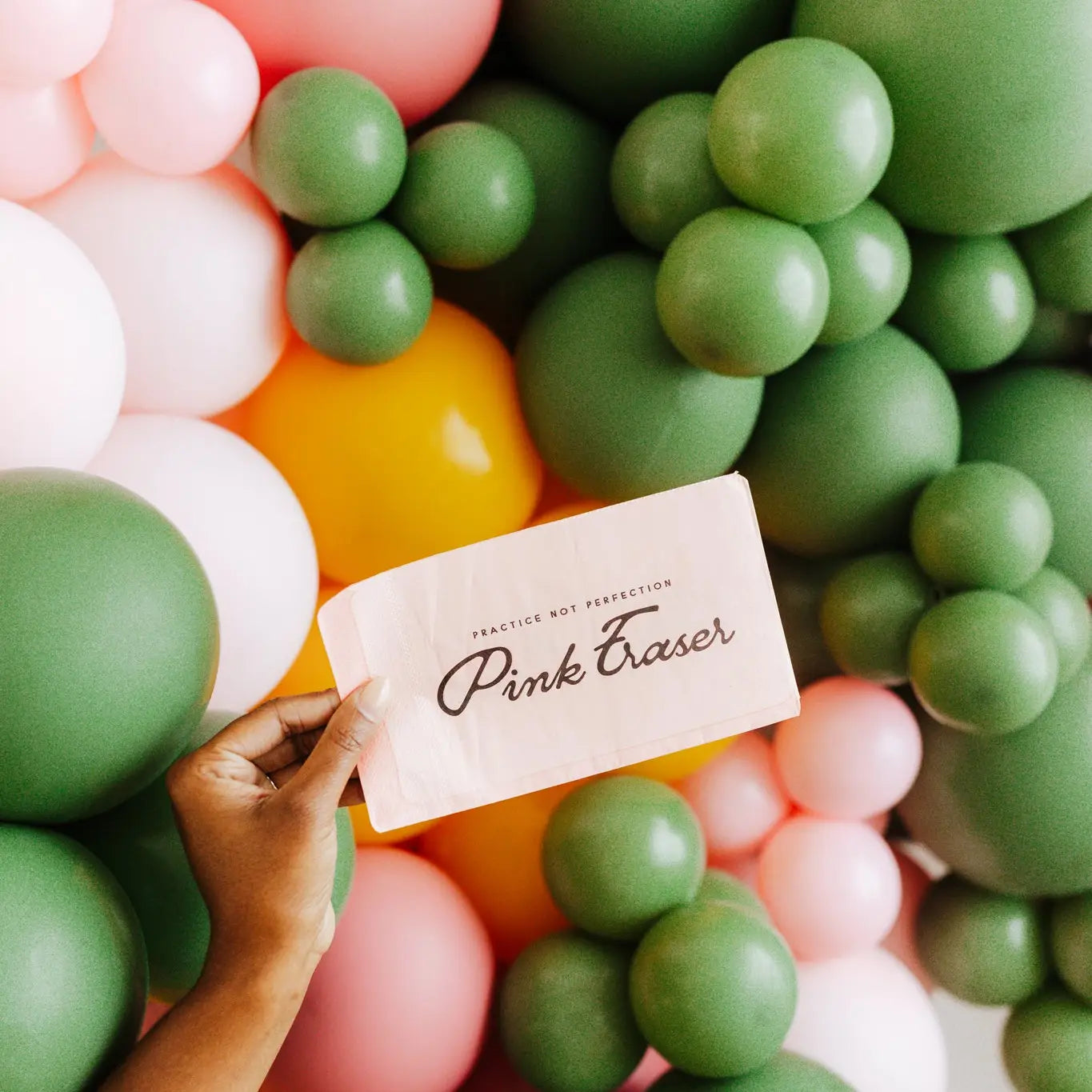 Hand holding a card with 'Pink Fraser' branding amidst colorful balloons