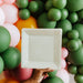 White square plate held in front of colorful balloons including green, pink, and orange.