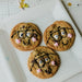 Three cookies decorated to look like characters with glasses and pink cheeks on a piece of paper.