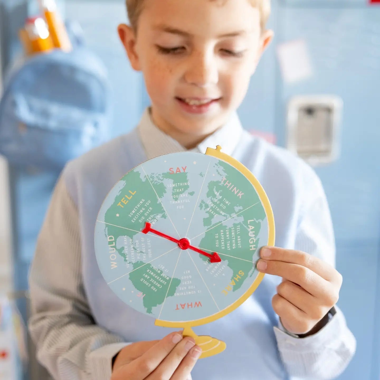Child holding a round world map with text and a red arrow, against a classroom background.