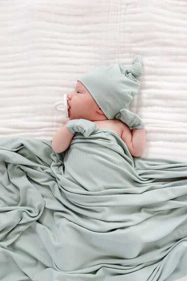 Newborn baby wrapped in a light green blanket and wearing a matching hat on a white background