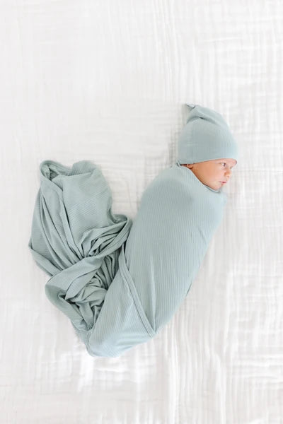 Newborn baby wrapped in a light green blanket and wearing a matching hat on a white background