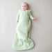 Baby wrapped in a light green sleep bag on a plain background