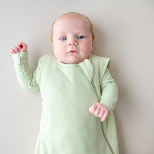 Baby wearing a light green sleep bag against a plain background