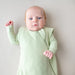 Baby wearing a light green sleep bag against a plain background
