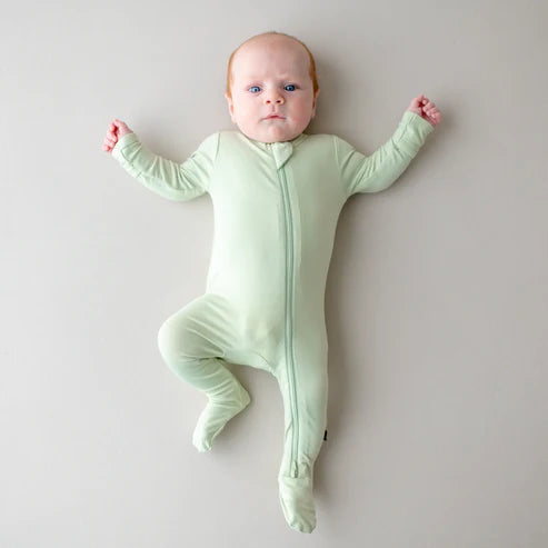 Baby wearing a light green zipper footie on a plain background