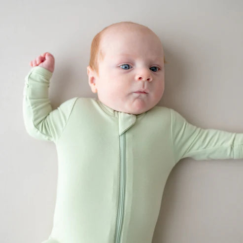 Baby wearing a light green zipper footie with a zipper on a plain background