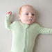 Baby wearing a light green zipper footie with a zipper on a plain background