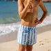 Person wearing blue and white striped swim shorts on a beach.