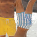Two people wearing colorful swim shorts on a beach.