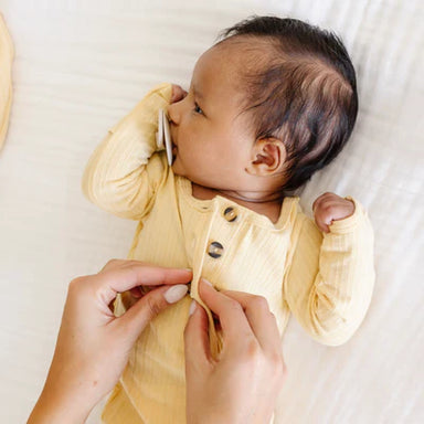 Baby in a yellow outfit with a person adjusting the clothing on a white background