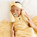 Newborn baby wrapped in yellow fabric with a pacifier, lying on a white blanket.