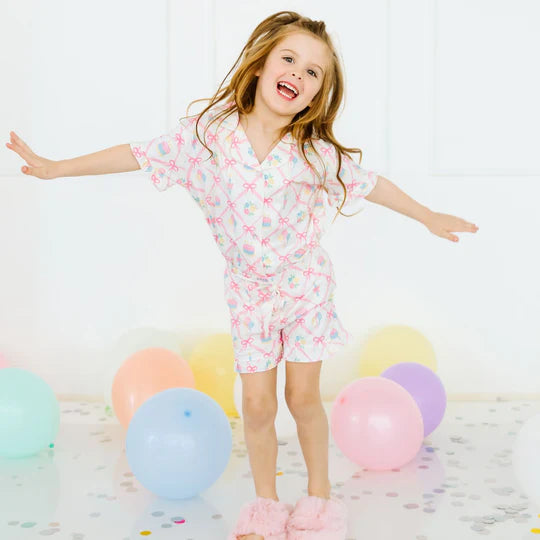 Young girl in a patterned outfit with colorful balloons and confetti on a light background
