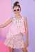 Young girl wearing a pink top and floral skirt with sunglasses against a pink and purple gradient background