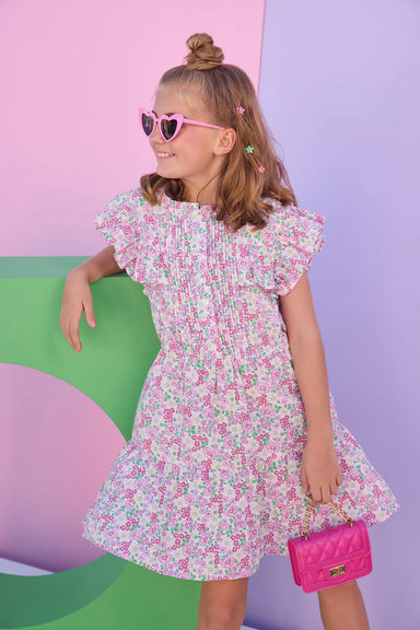 Young girl in a floral dress with pink sunglasses and a pink clutch against a colorful background