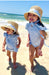 Two children in matching blue outfits and straw hats on a beach.