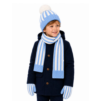 A young boy wearing a matching winter outfit with a navy blue coat, a light blue and white striped knit beanie with a pom-pom, a matching striped scarf, and striped knit mittens, photographed against a solid white background.